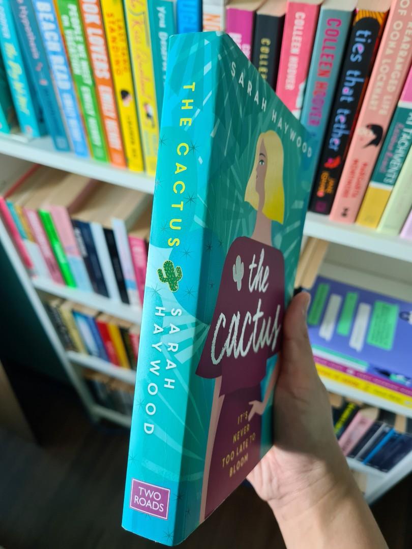 Paperback edition of The Cactus by Sarah Haywood resting on a wooden surface