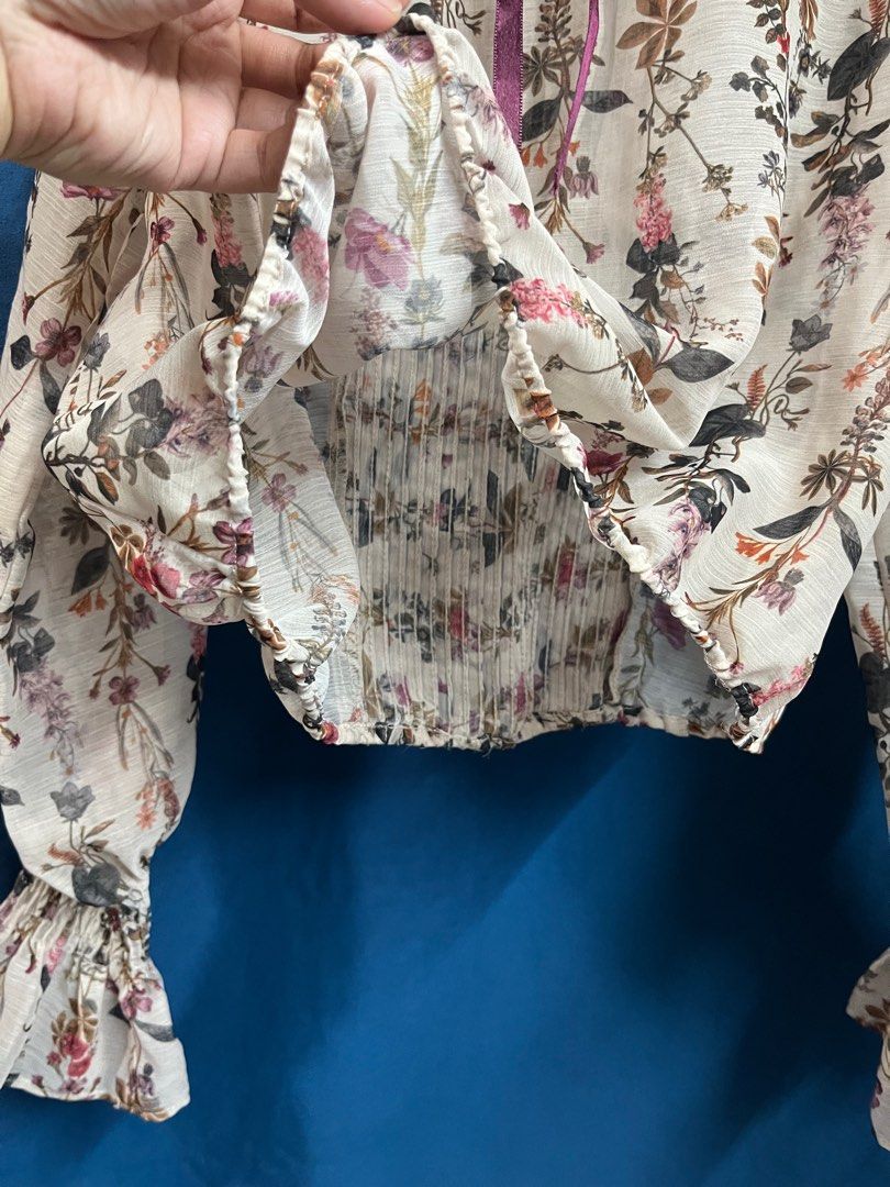 Zara Basic Cream Semi-sheer Floral Longsleeve Top (Category: Blouses) located in Quezon City. Submitted by wednesday21 (Listing ID 1335114463, Image 3). Description: Cream floral blouse with ruffled neckline and pleated design in front. Long sleeves with garterized, ruffled cuffs. Semi-cropped length in semi-sheer fabric and keyhole purple ribbon tie at the back. With delicate floral pattern in muted colors. Can fit XS-S. 3-day reservation only. 