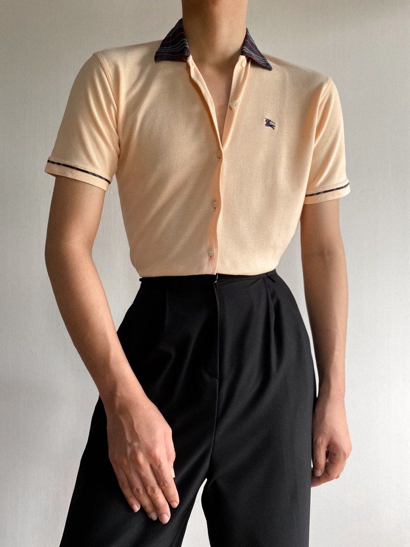 Burberry Button up Short Sleeves Shirt (Category: Luxury Apparel) located in Cordon. Submitted by theclassic (Listing ID 1287853483, Image 3). Description: True vintage waffle closed button up style Burberry short sleeves shirt with iconic plaid style collar and sleeves hem lining. A subtle peach to apricot tone features classic equestrian knight chest embroidered logo. Has tiny color transfer. Made in England. Best fit small body frames. P • 139