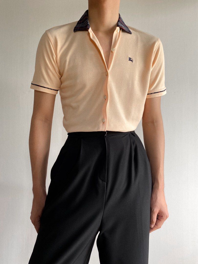 Burberry Button up Short Sleeves Shirt (Category: Luxury Apparel) located in Cordon. Submitted by theclassic (Listing ID 1287853483, Image 2). Description: True vintage waffle closed button up style Burberry short sleeves shirt with iconic plaid style collar and sleeves hem lining. A subtle peach to apricot tone features classic equestrian knight chest embroidered logo. Has tiny color transfer. Made in England. Best fit small body frames. P • 139