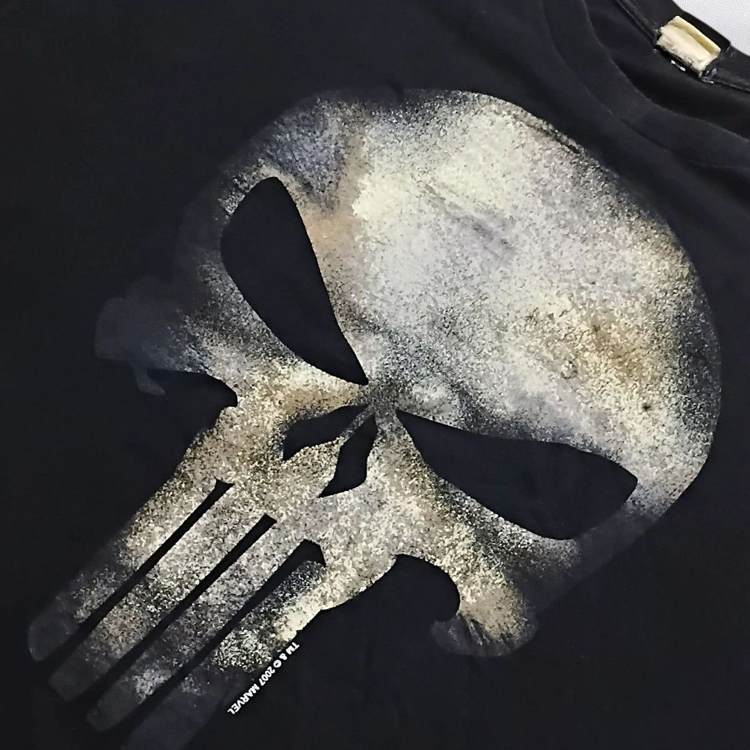 (GRAILED PIECE) MAD ENGINE Punisher, dated back to 2007. (Category: Tshirts & Polo Shirts ) located in Caloocan City. Submitted by dyn0zx (Listing ID 1397951649, Image 2). Description: (GRAILED PIECE) MAD ENGINE Punisher, dated back to 2007. Dimensions: Width: 24 Length: 32 This Punisher t-shirt features a striking, distressed graphic of the Punisher's skull logo in shades of grey, white, and subtle gold or tan, giving it a gritty, worn appearanc