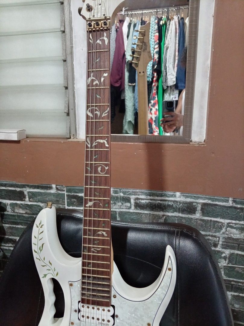 Ibanez Jem Electric Guitar (Category: Musical Instruments) located in Agdangan. Submitted by hairulmusicalcolection (Listing ID 1397856044, Image 2). Description: White Ibanez Jem electric guitar. Features a pearlescent pickguard and floral inlay on the fretboard. The body has a floral design. Includes gold hardware and a tremolo system. The headstock has the Ibanez logo. The guitar has two knobs and three pickups..