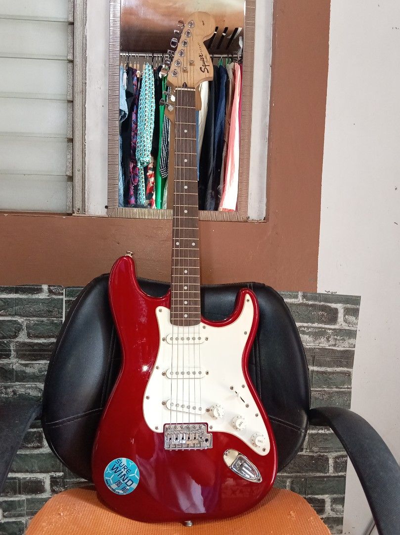 Squier Stratocaster Electric Guitar (Category: Musical Instruments) located in Agdangan. Submitted by hairulmusicalcolection (Listing ID 1397823346, Image 1). Description: - Red Squier Stratocaster electric guitar - White pickguard - Three single-coil pickups - Squier and Fender headstock logos - Includes a sticker on the body.