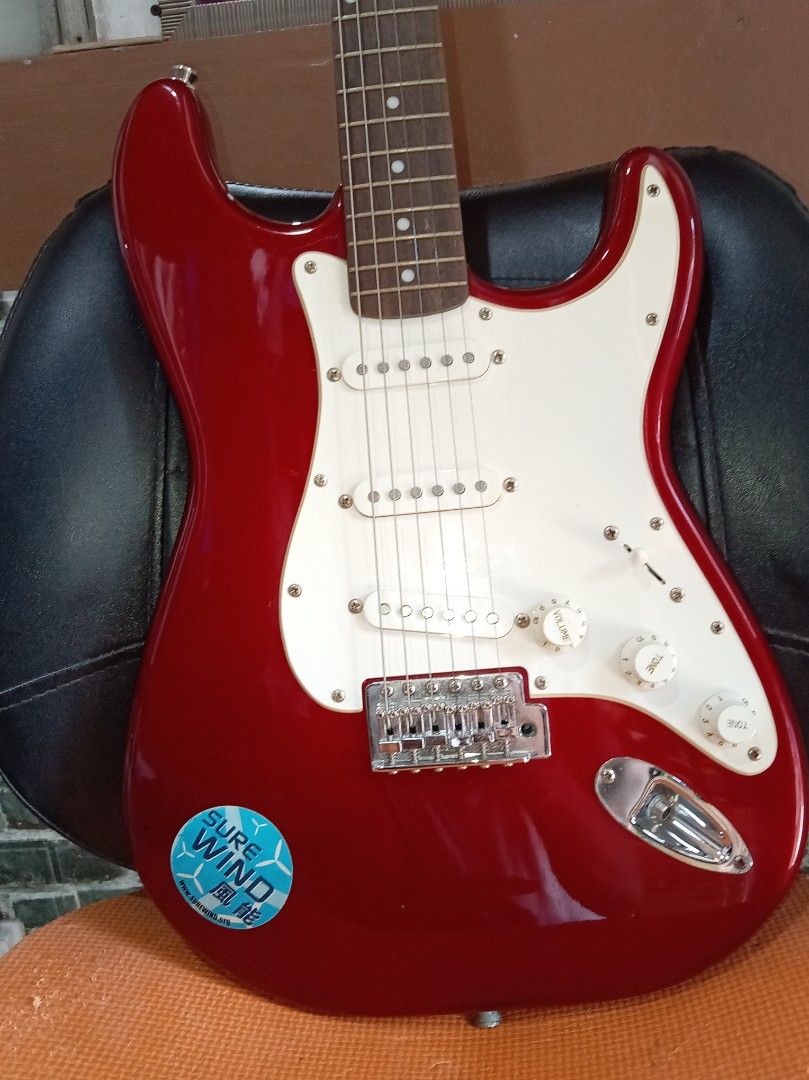 Squier Stratocaster Electric Guitar (Category: Musical Instruments) located in Agdangan. Submitted by hairulmusicalcolection (Listing ID 1397823346, Image 2). Description: - Red Squier Stratocaster electric guitar - White pickguard - Three single-coil pickups - Squier and Fender headstock logos - Includes a sticker on the body.