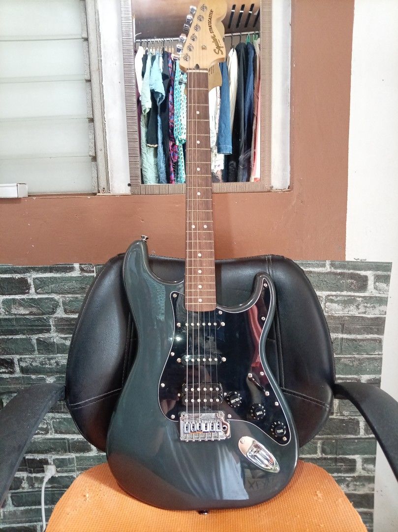 Squier Stratocaster Electric Guitar (Category: Musical Instruments) located in Agdangan. Submitted by hairulmusicalcolection (Listing ID 1397824379, Image 1). Description: - Squier Stratocaster electric guitar - Dark grey body - Black pickguard - Chrome hardware - Squier Stratocaster headstock logo - Volume and tone controls.