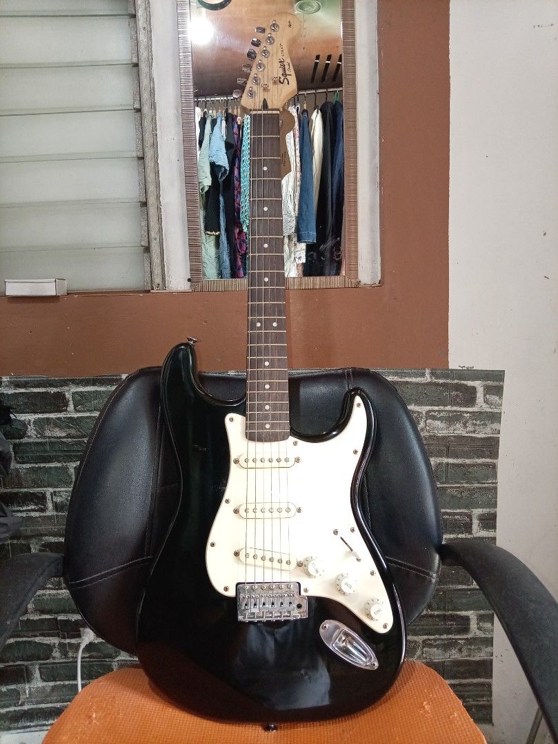 Squier Stratocaster Electric Guitar (Category: Musical Instruments) located in Agdangan. Submitted by hairulmusicalcolection (Listing ID 1397835678, Image 1). Description: - Black Squier Stratocaster electric guitar - White pickguard - Three single-coil pickups - Tremolo bridge - Squier and Fender logos on headstock - Black body with white electronics cover - Maple neck.
