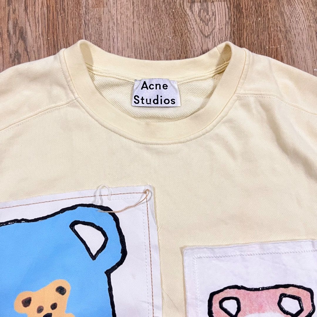 Acne Studios Sweatshirt (Category: Luxury Apparel) located in Bacolod City. Submitted by boujee.wardrobes (Listing ID 1398155542, Image 3). Description: - Cream-colored Acne Studios sweatshirt - Features two front patches: teddy bear design with Acne Studios logo and floral design with Acne Studios logo - Made in Portugal Acne Studios by Grant Levy Lucero Bear Vase Patches XS on tag Length: 27 Width: 25.