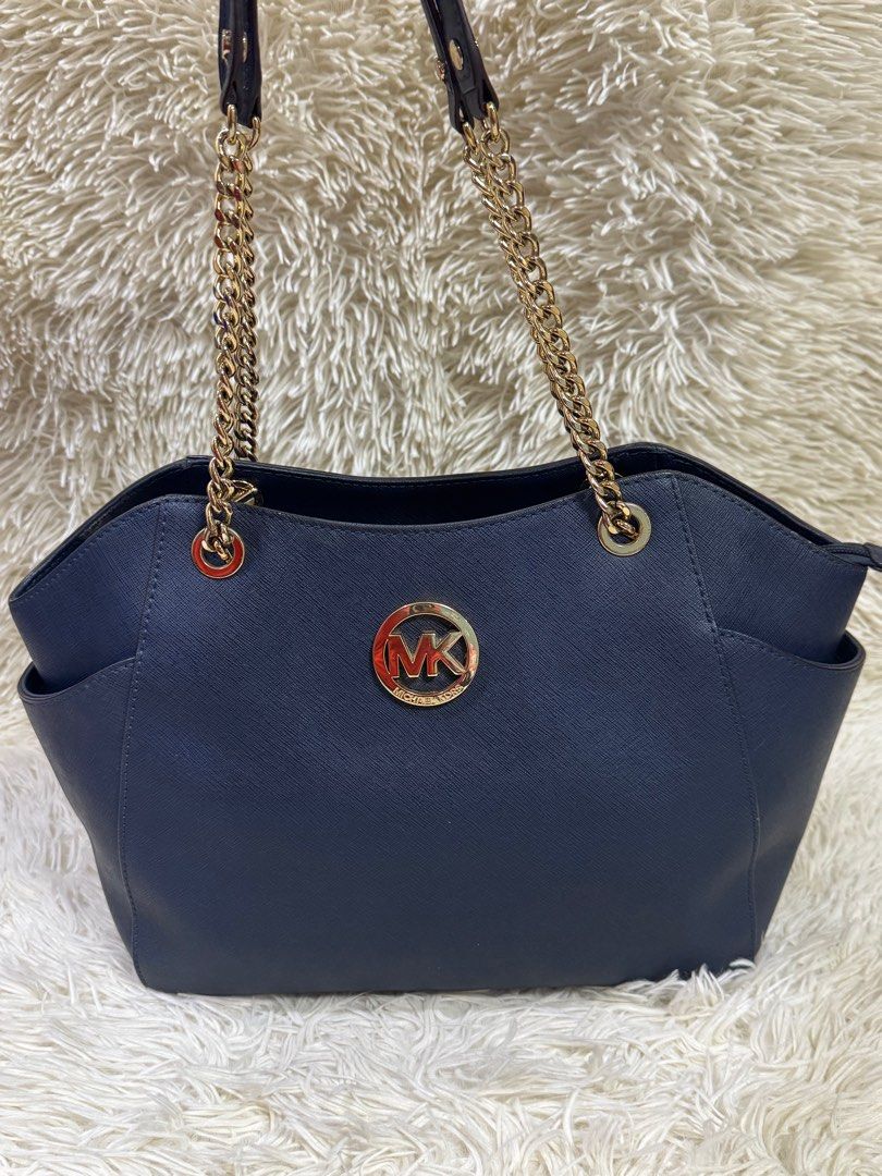 Michael Kors Navy Blue Tote Bag (Category: Luxury Bags & Wallets) located in Rodriguez. Submitted by nancyb13 (Listing ID 1397985011, Image 2). Description: - Michael Kors navy blue tote bag - Gold-tone chain straps - Gold MK logo - Zippered main compartment - Multiple interior pockets - Side pockets - Structured base - Branded interior lining.