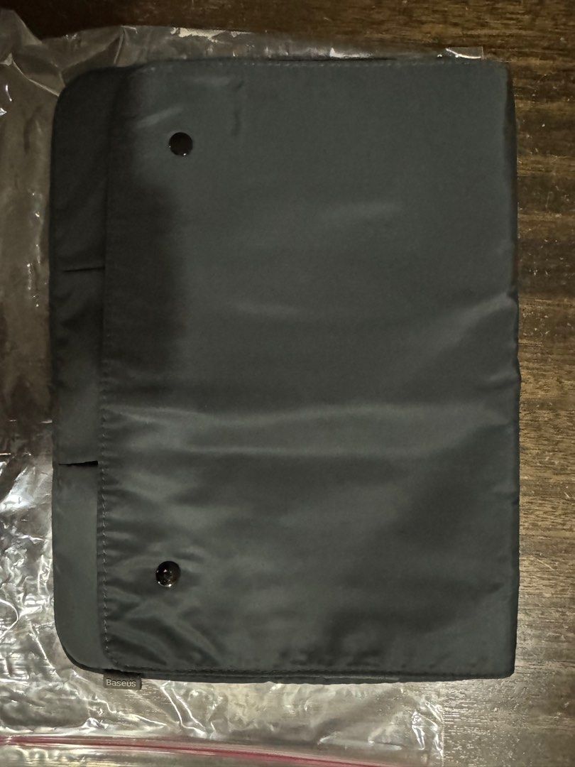 Baseus Laptop Sleeve (Category: Laptop Bags & Sleeves) located in Quezon City. Submitted by vsaint (Listing ID 1398270572, Image 1). Description: - Dark gray Baseus laptop sleeve - Flap closure with two snap buttons - Multiple interior pockets for accessories - Made of smooth, potentially water-resistant material - Provides stylish laptop protection.
