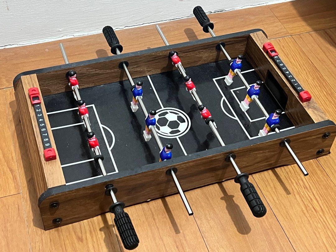 Mini Foosball Table (Category: Board Games & Puzzles) located in Cavite. Submitted by nlp_preloved (Listing ID 1398287952, Image 1). Description: - Mini foosball table for home entertainment. - Features a wooden frame and black playing surface. - Includes red and blue player figures. - Comes with score counters. - Compact and easy to store. - Ideal for small spaces..