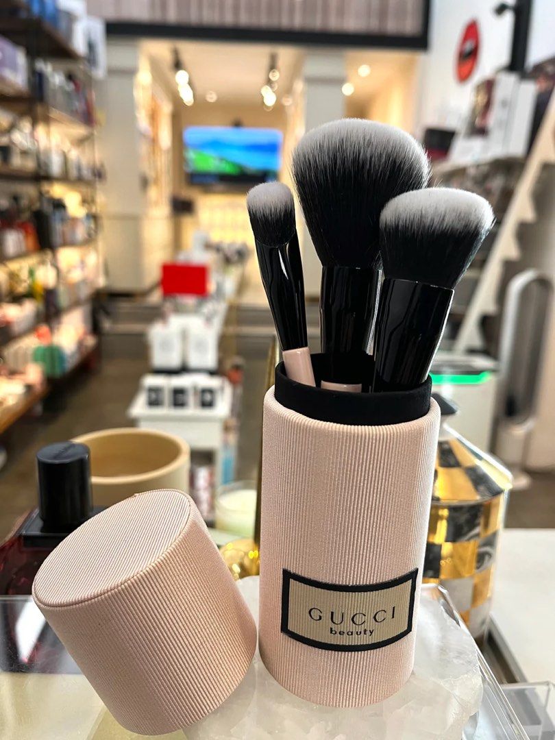 Gucci Beauty Makeup Brush Set (Category: Makeup) located in Manila. Submitted by rockinpart49318 (Listing ID 1398801262, Image 1). Description: - Authentic Gucci Beauty makeup brush set. - Includes multiple brushes of different sizes and shapes. - Features black handles and white bristles. - Comes with a pink cylindrical container. - Container has a matching lid. - Gucci Beauty logo is present on the container..