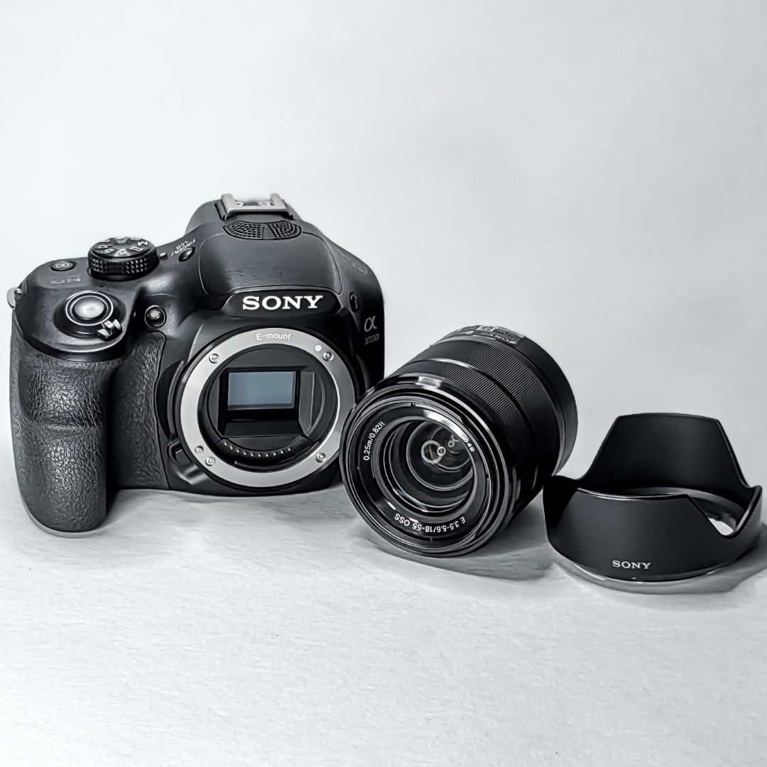 Sony Alpha a3000 Mirrorless Camera with Lens (Category: Cameras) located in Balanga. Submitted by cyrin_camera (Listing ID 1398999608, Image 3). Description: - Sony Alpha a3000 mirrorless camera with E 3.5-5.6/18-55 OSS lens. - Includes: lens hood, camera bag, strap, battery, charger, and USB adapter. - Features a mode dial for various shooting settings. - Built-in flash and display screen. - Lens has a focus ring and lens cap..