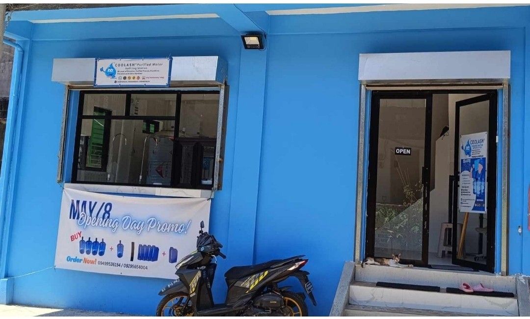 For rent commercial space include water station (Category: Apartments & Condos) located in Caloocan City. Submitted by latrinaavi (Listing ID 1399309636, Image 1). Description: Commercial space available for lease. Features a modern interior with a kitchen area and ample open space. The exterior showcases a blue facade with a storefront, suitable for various business types. Includes a waiting area and a clean, well-lit environment. Perfect for es