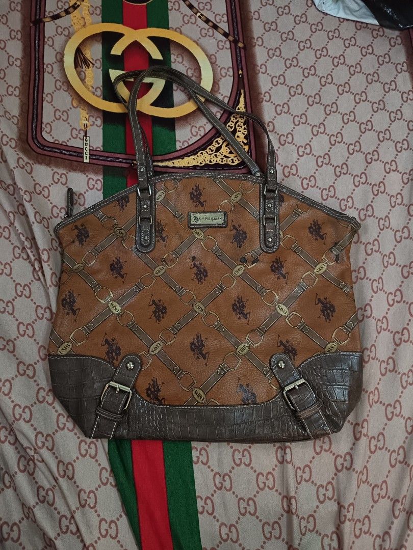 US Polo Assn. Brown Tote Bag (Category: Tote Bags) located in Paracelis. Submitted by blessed_.0 (Listing ID 1399258937, Image 1). Description: - US Polo Assn. tote bag - Brown color with patterned design - Crocodile-textured bottom - Features two top handles - Zipper closure - Interior pocket - Brown and gold color scheme - Structured shape.