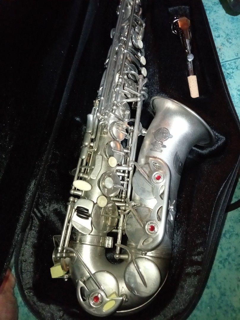 Mark RETHYM Golden Wind Saxophone (Category: Musical Instruments) located in Agdangan. Submitted by hairulmusicalcolection (Listing ID 1399705548, Image 3). Description: - Mar RETHYM Golden Wind Saxophone - Silver finish - Model: DV-850 - Includes: Case, mouthpiece, and cork - Black case with red trim - Features keys and buttons.