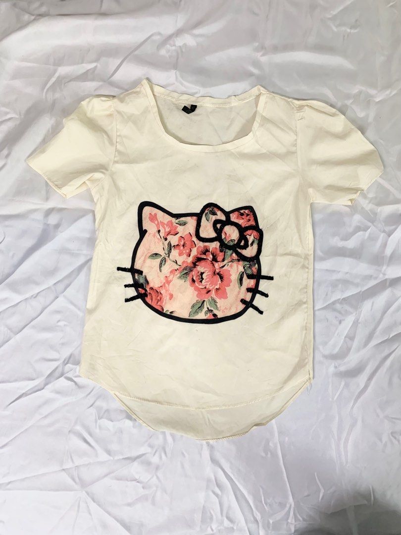 Hello Kitty Floral Print T-shirt (Category: Shirts) located in Manila. Submitted by jjaness (Listing ID 1399900194, Image 1). Description: Cream-colored t-shirt featuring a Kitty design with a floral print. The design is outlined in black and has beaded accents. It has short sleeves and a rounded hem..