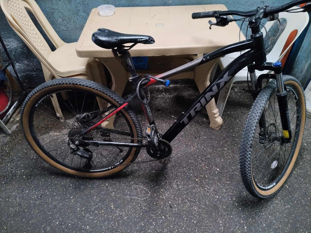 Trinx Mountain Bike (Category: Bicycles) located in Manila. Submitted by siredzelsa30772 (Listing ID 1400267505, Image 2). Description: Black Trinx mountain bike with tan tires. Features front suspension and disc brakes. The bike has a black frame with red accents. Includes a black seat and handlebars..