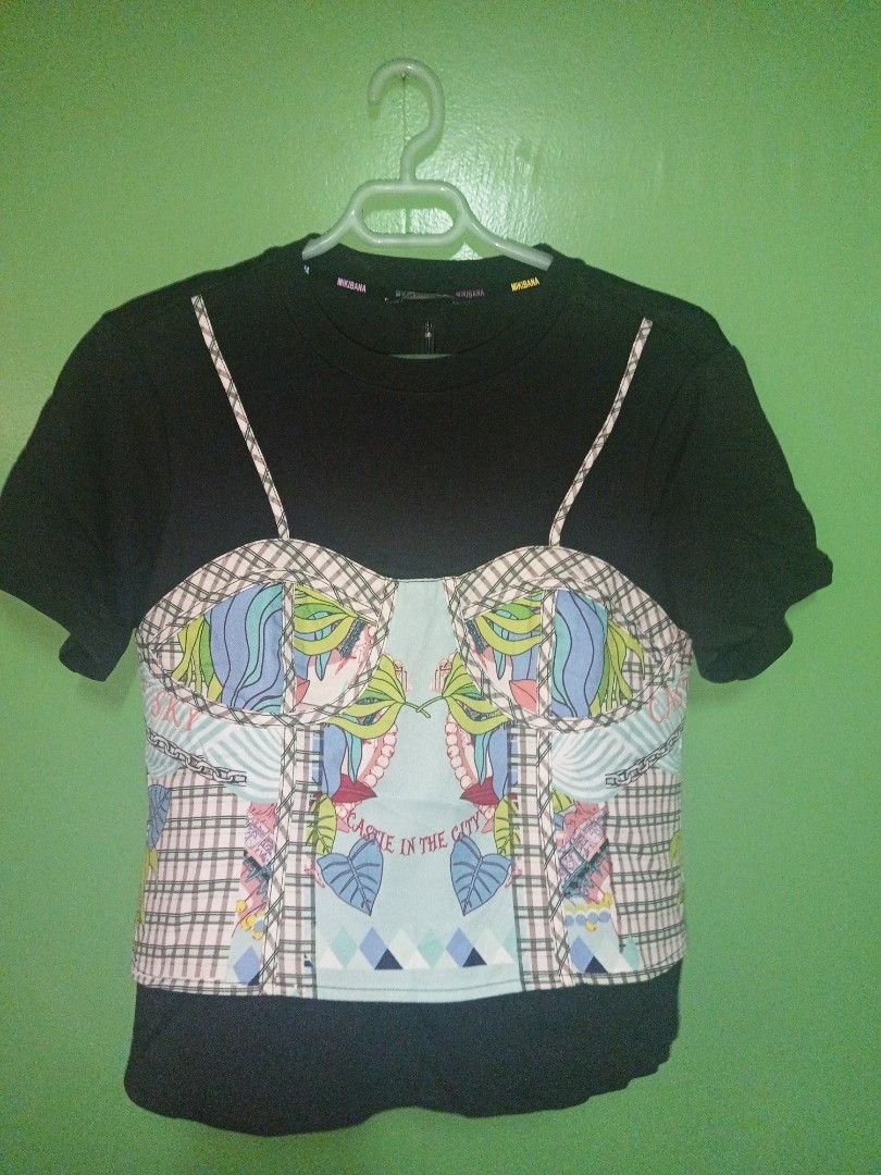Black T-shirt with Printed Bustier (Category: Shirts) located in Rizal. Submitted by judithtillo19 (Listing ID 1400529647, Image 2). Description: Black t-shirt features a unique printed bustier design. The bustier has a colorful pattern with a plaid design on the sides and a central design with the text "A PLACE IN THE CITY". The back of the shirt has a plaid design. It has short sleeves and a round neckline..