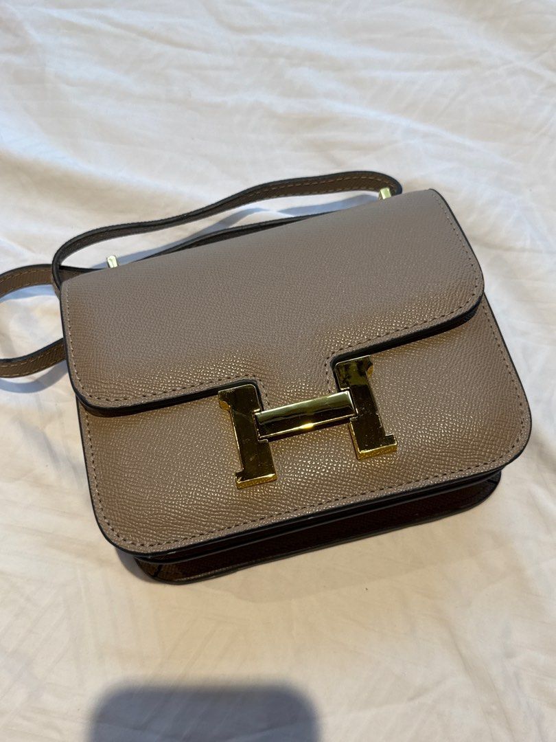 Hermes Mini Constance Bag (Category: Luxury Bags & Wallets) located in Manila. Submitted by cathylimmm (Listing ID 1400527342, Image 2). Description: READ FIRST! Beautiful Hermes Mini Constance bag in a neutral taupe color. Features a gold-tone 'H' clasp and a matching shoulder strap. The interior is lined with leather and includes a small pocket. The bag's design is structured, with a flap closure. Size 18 -korea sourced (not guaranteed) -flaws 