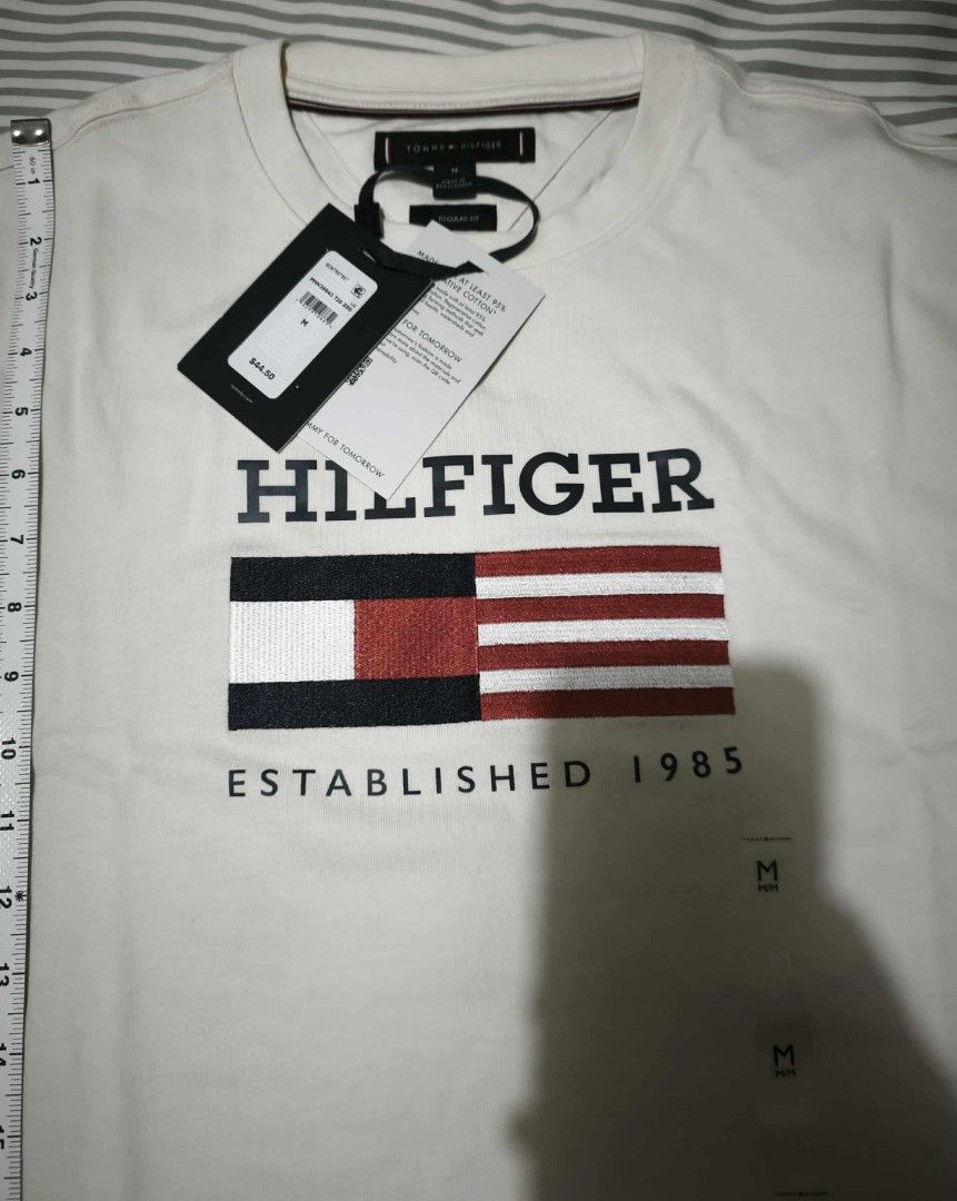 Tommy Hilfiger Flag Logo T-shirt - Medium (Category: Tshirts & Polo Shirts ) located in Paranaque City. Submitted by k_declutters (Listing ID 1400491064, Image 2). Description: - Authentic Tommy Hilfiger T-shirt - Features the iconic Hilfiger flag logo - Color: White - Neckline: Crew neck - Size: Medium - Condition: New with tags (NWT) - Still in original packaging.