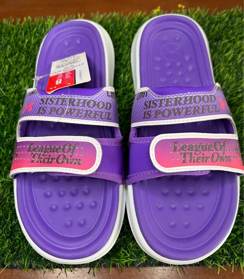 Under Armour UA W Ansa Studio IWD SL Slides (Category: Slippers and slides) located in Manila. Submitted by phatpen (Listing ID 1400450340, Image 1). Description: These Under Armour slides feature a purple and white design with the words "Sisterhood is Powerful" and "League of Their Own". size 8 US,. The slides are new with the original tag still attached, showing a price of $49.99..