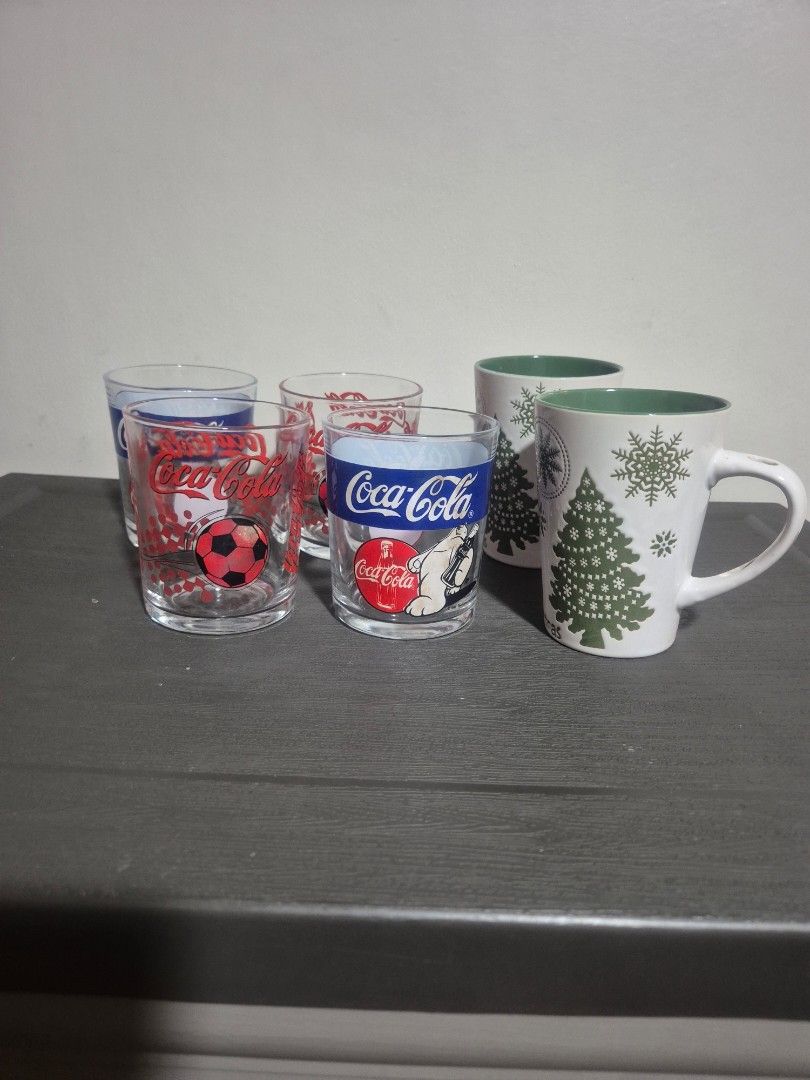 Christmas Mugs and Coca-Cola Glasses Set (Category: Coffee & Tea Tableware) located in Pasig City. Submitted by rubyspick (Listing ID 1400650320, Image 3). Description: Set includes two Christmas-themed mugs with snowflake and tree designs, and three Coca-Cola glasses. The mugs have a white exterior and green interior. The Coca-Cola glasses feature various designs, including a polar bear and a soccer ball. Perfect for adding a festive touch to yo