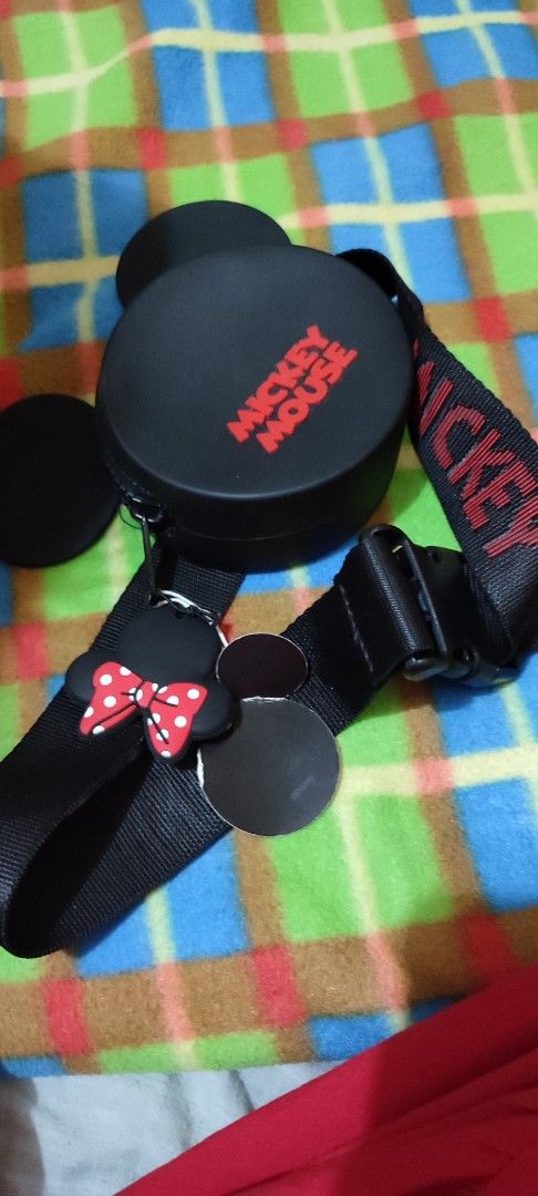 Mickey Mouse Round Bag with Strap (Category: Carriers & Slings) located in Manila. Submitted by dsanjuansdeclutter2 (Listing ID 1400755637, Image 2). Description: Round bag features a Mickey Mouse design with attached ears and a strap. The bag has a zipper closure and a Mickey Mouse charm with a red bow. The strap is black with the word "Mickey" printed on it. The bag is black with the words "Mickey Mouse" printed in red..