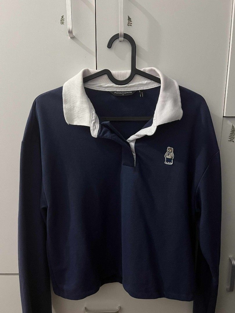 Penshoppe Crop Long Sleeve (Category: Tshirts & Polo Shirts ) located in General Trias. Submitted by pepperbits (Listing ID 1400789428, Image 1). Description: - Color: Navy blue - Features a white collar - Small embroidered logo on the chest - Long-sleeved - Button-up neckline - Cropped style - Plain navy blue back.