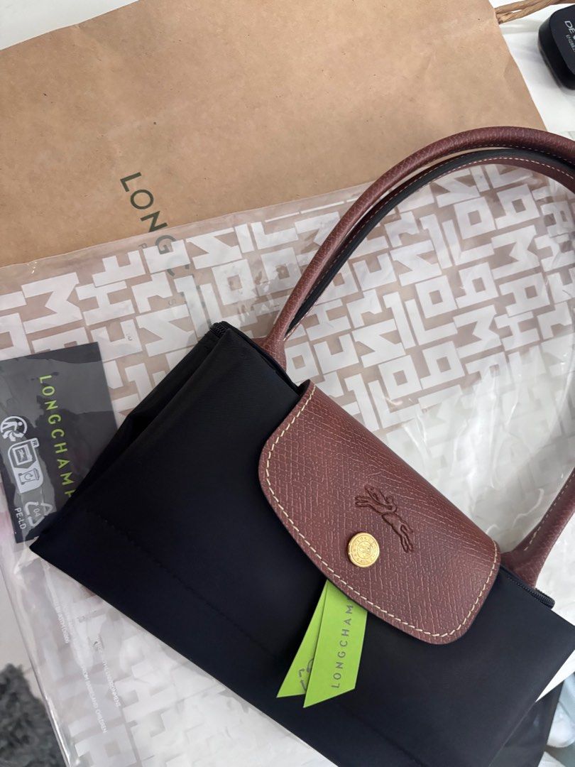 Longchamp Long handle medium black (Category: Luxury Bags & Wallets) located in Quezon City. Submitted by aloracollections_ (Listing ID 1401154108, Image 2). Description: - Authentic Longchamp Le Pliage handbag - Color: Black with brown leather accents - Features flap closure with gold-tone button and Longchamp logo - Includes original tags - New and unused condition - Still in original packaging.