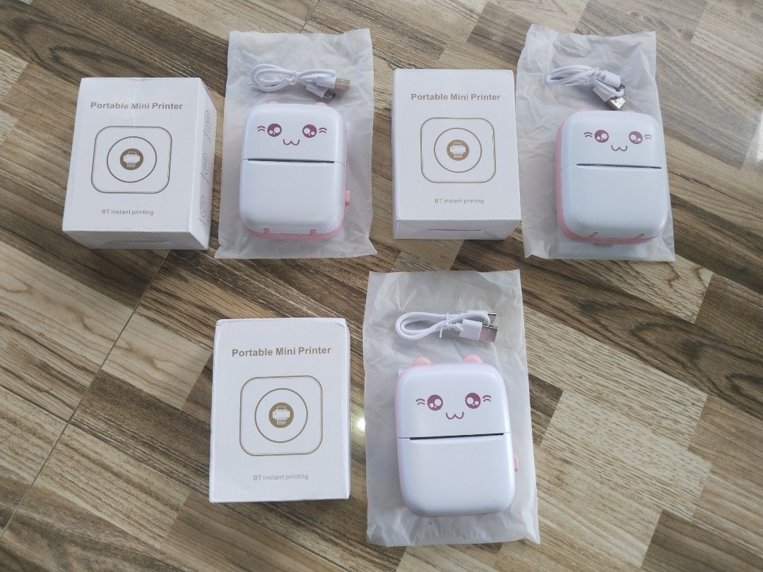Portable Mini Printer - Cute Design (Category: Printers, Scanners & Copiers) located in San Luis. Submitted by thrift.with.shey (Listing ID 1401057669, Image 1). Description: Portable mini printer features a cute design. It comes with a charging cable and is packaged in its original box. The printer has a white and pink color scheme. The design includes a smiling face with cat ears..