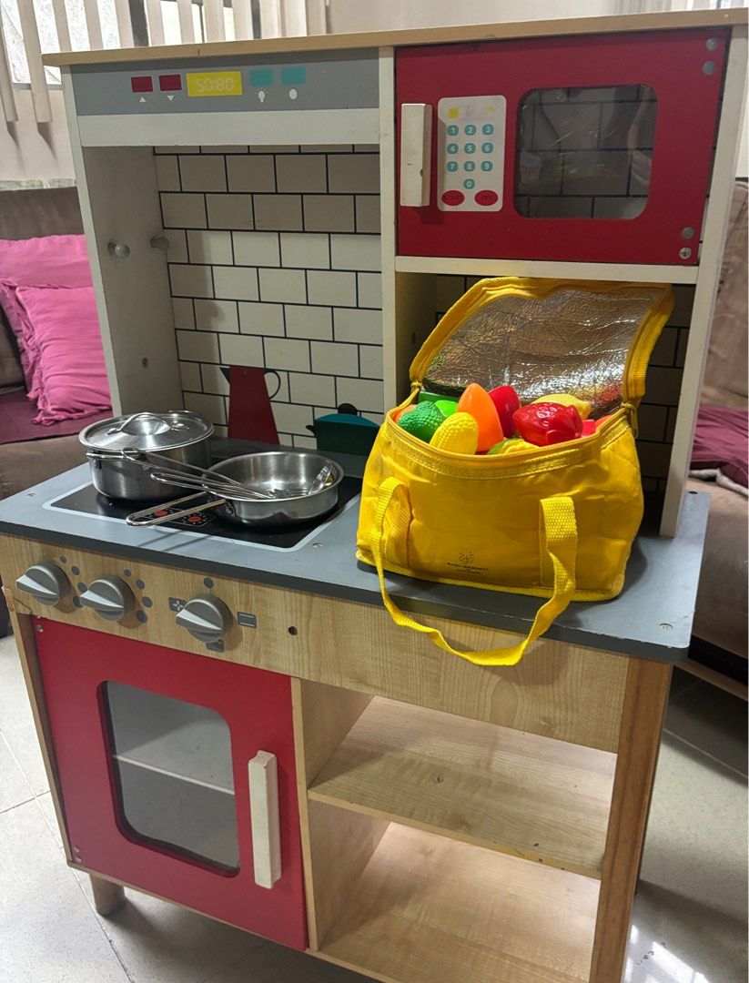 Wooden Play Kitchen Set with Accessories (Category: Kids Toys) located in Bacoor. Submitted by cabscloset (Listing ID 1401054973, Image 2). Description: - Wooden play kitchen with stove, oven, microwave, and sink. - Includes pots, pans, and play food. - Features knobs and a faucet. - Red oven door. - Light wood finish with gray countertop and white brick backsplash. *** Please note the defect on the red door.
