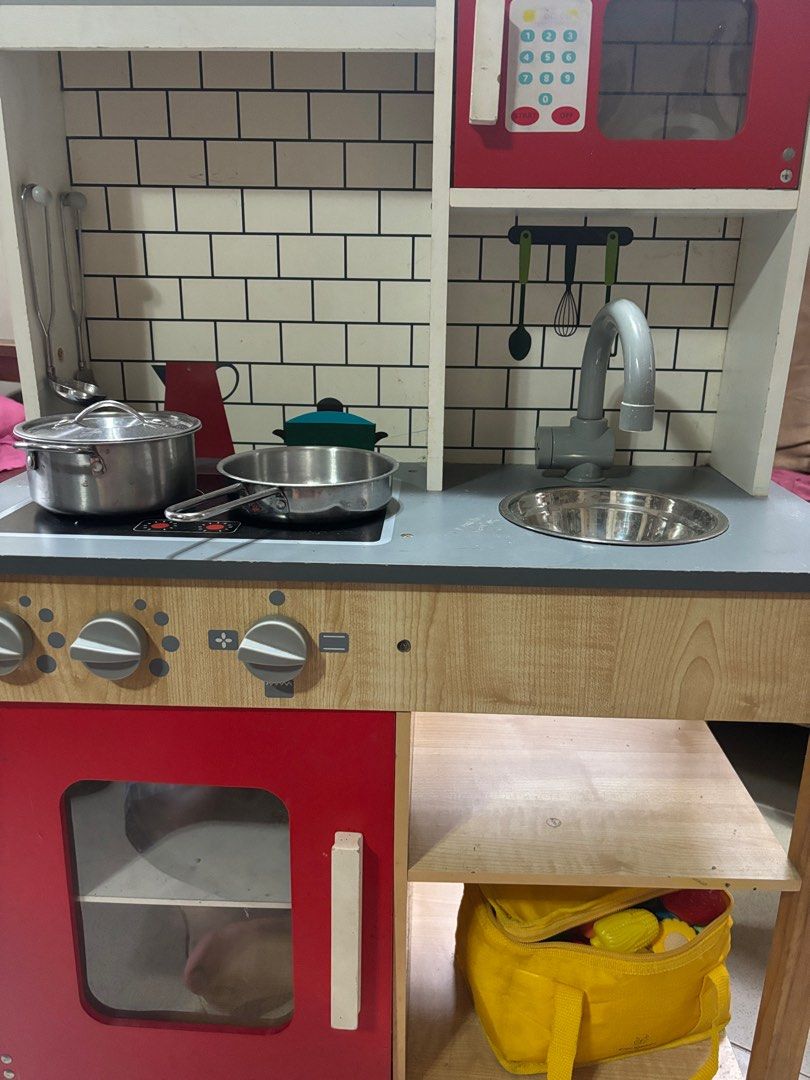 Wooden Play Kitchen Set with Accessories (Category: Kids Toys) located in Bacoor. Submitted by cabscloset (Listing ID 1401054973, Image 3). Description: - Wooden play kitchen with stove, oven, microwave, and sink. - Includes pots, pans, and play food. - Features knobs and a faucet. - Red oven door. - Light wood finish with gray countertop and white brick backsplash. *** Please note the defect on the red door.
