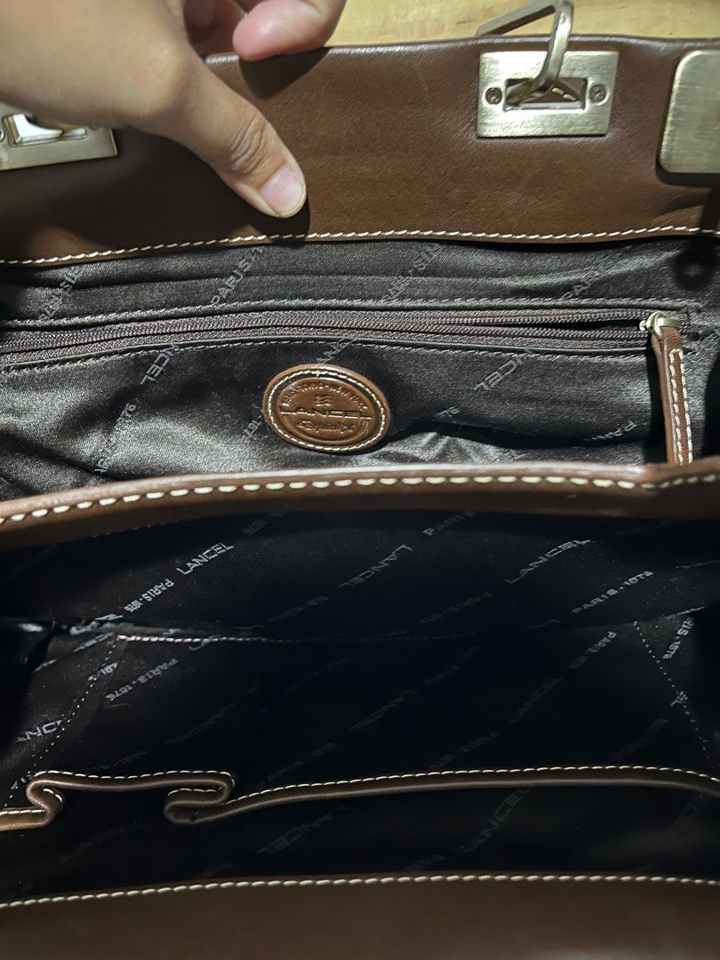 Lancel Paris Brown Handbag (Category: Luxury Bags & Wallets) located in San Fernando. Submitted by gemsfndr (Listing ID 1396257332, Image 3). Description: - Lancel Paris handbag - Dual-tone brown design - Lighter brown suede-like material on front pockets - Top handle - Zip closure - Dark brown fabric interior lining with Lancel Paris logo - Multiple compartments - Metal clasp closure.