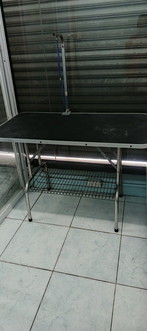 Pet Grooming Table with Adjustable Arm (Category: Homes & Other Pet Accessories) located in Quezon City. Submitted by marizalyanna (Listing ID 1396165412, Image 1). Description: - Black, textured tabletop - Sturdy metal frame - Adjustable grooming arm with blue restraint loop - Wire mesh shelf for storage - Perfect for various pet grooming tasks Loc: cubao 110x60.