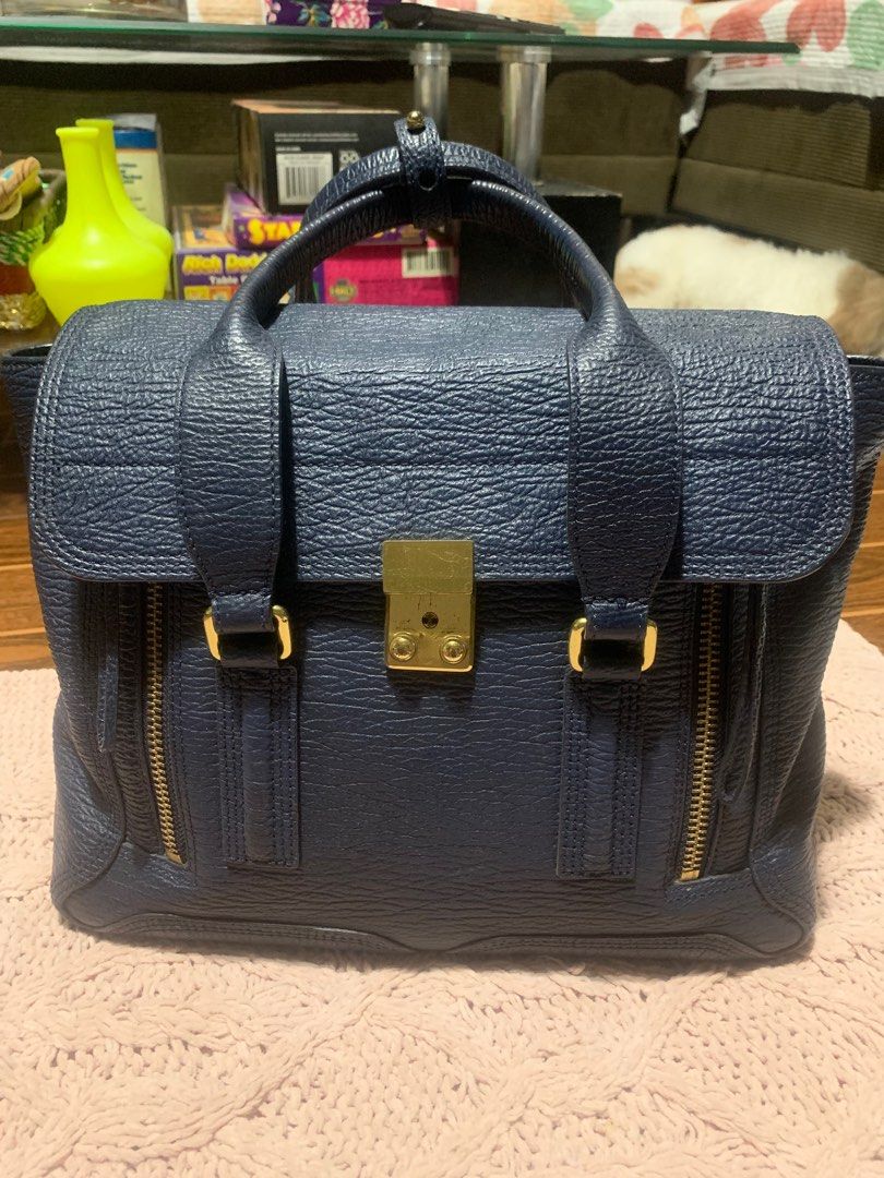 3.1 Phillip Lim Navy Leather Satchel (Category: Luxury Bags & Wallets) located in Bulacan. Submitted by love2loved (Listing ID 1401308643, Image 1). Description: Navy blue leather satchel bag from 3.1 Phillip Lim. Features a top handle, a flap closure with a gold-tone clasp, and gold-tone hardware. Includes two exterior zip pockets and a spacious interior. The interior has a zip pocket with the brand's logo. The zipper has a YKK logo. The bag has