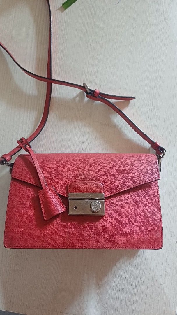 Prada Red Crossbody Bag (Category: Luxury Bags & Wallets) located in Lemery. Submitted by venus23 (Listing ID 1401484272, Image 1). Description: prada crossbody bag features a vibrant red exterior with a unique textured finish. It has a flap closure with a metal clasp. The bag includes a detachable strap and multiple compartments inside. The interior is black with a red lining. The bag has a small stain on the front. The bag has a tag with the nu