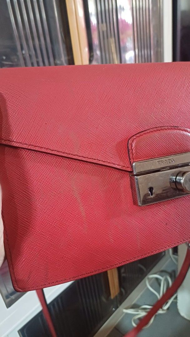 Prada Red Crossbody Bag (Category: Luxury Bags & Wallets) located in Lemery. Submitted by venus23 (Listing ID 1401484272, Image 2). Description: prada crossbody bag features a vibrant red exterior with a unique textured finish. It has a flap closure with a metal clasp. The bag includes a detachable strap and multiple compartments inside. The interior is black with a red lining. The bag has a small stain on the front. The bag has a tag with the nu