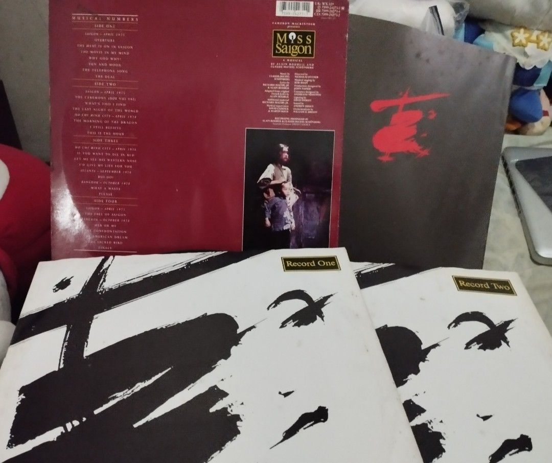 Miss Saigon Vinyl Record Set (Category: Vinyls) located in Paranaque City. Submitted by myprelovedbutlovedshop (Listing ID 1396728963, Image 2). Description: - Miss Saigon vinyl record set. - Includes multiple records. - Features the songs "Saigon" and "Record One." - Album cover with a striking helicopter silhouette against a sunset. - Back of the album includes the tracklist. - Includes a photo of a performer..