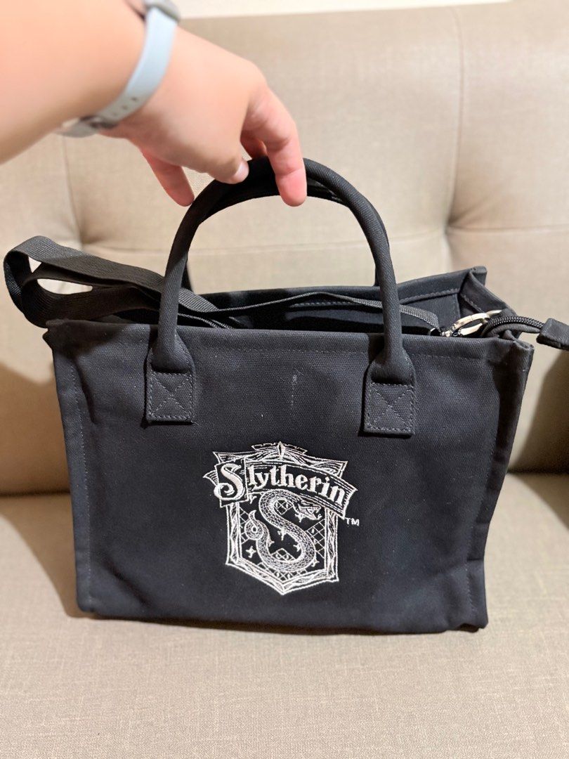 Gracegift Slytherin Tote Bag with Shoulder Strap (Category: Tote Bags) located in Marikina City. Submitted by savedbygracephb (Listing ID 1396912713, Image 1). Description: - Black Slytherin tote bag - Top handle and detachable shoulder strap (replaced) - Zippered main compartment - Small inner pocket - Gold-colored charm on zipper pull - Gracegift label - Canvas material.