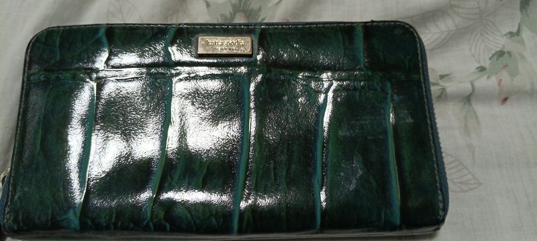 Kate Spade Green Wallet (Category: Wallets & Card holders) located in Calamba. Submitted by mel013 (Listing ID 1397053926, Image 1). Description: - Kate Spade green wallet - Rectangular shape - Secure zip closure - Stylish textured surface with vertical pleats - Features a small, branded metal plate - Made from a glossy material.