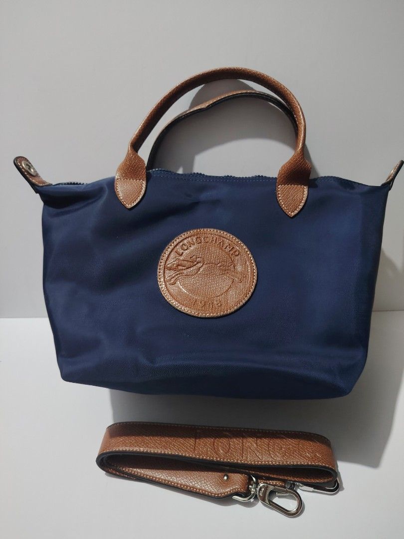 NOT OG Longchamp Le Pliage Handbag with Shoulder Strap (Category: Luxury Bags & Wallets) located in Valenzuela. Submitted by ryu12 (Listing ID 1397099333, Image 1). Description: - Not OG Navy blue Longchamp Le Pliage handbag - Brown leather handle - Detachable shoulder strap - Zip closure - Spacious interior - Longchamp logo on front - Interior pocket.