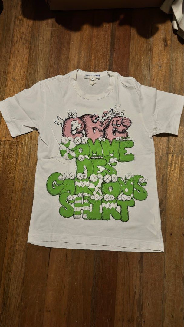 Comme des Garcons Shirt x KAWS Graphic Tee (Category: Luxury Apparel) located in Quezon City. Submitted by area008 (Listing ID 1401655588, Image 1). Description: Kaws x Comme des Garçons white graphic shirt AUTHENTIC CONDITION 9.5/10 May stain sa left top shoulder pero not permanent damage.