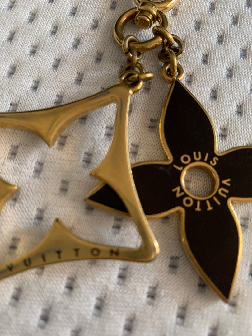 Louis Vuitton Key Chain (Category: Luxury Accessories) located in Rodriguez. Submitted by mbongscloset (Listing ID 1401548861, Image 2). Description: Louis Vuitton key chain features a gold-tone finish with two charms. One charm is a flower shape with the Louis Vuitton logo, and the other is the LV logo. The key chain has a clasp for easy attachment to bags or keys. A stylish accessory to add a touch of luxury..