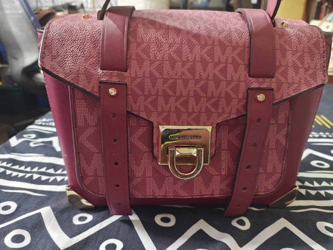 Michael Kors Handbag (Category: Luxury Bags & Wallets) located in Tabuk. Submitted by pinklarce (Listing ID 1401590807, Image 3). Description: - Authentic Michael Kors handbag - Color: Burgundy - Features the MK logo pattern - Gold-tone clasp with Michael Kors engraving - Includes a detachable strap - Made of a textured material -100 % Original.