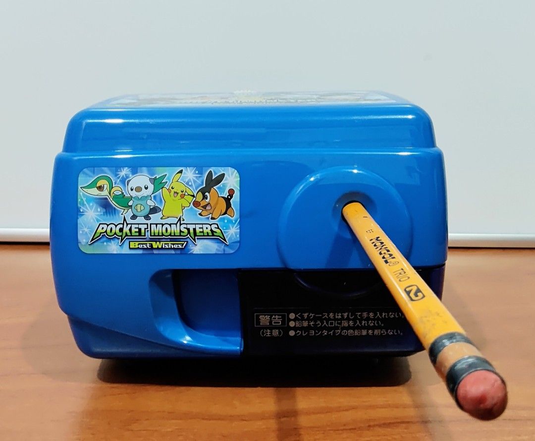 Pokemon Electric Pencil Sharpener (Category: Character Goods) located in Binangonan. Submitted by caaaris (Listing ID 1401669816, Image 3). Description: Electric pencil sharpener featuring a Pokemon design. It has a blue body with Pokemon graphics on the top and front. The sharpener has a pencil insertion hole and a compartment for shavings. It includes a power cord and a plug. The bottom has suction cups for stability. 100 volts. The model numbe