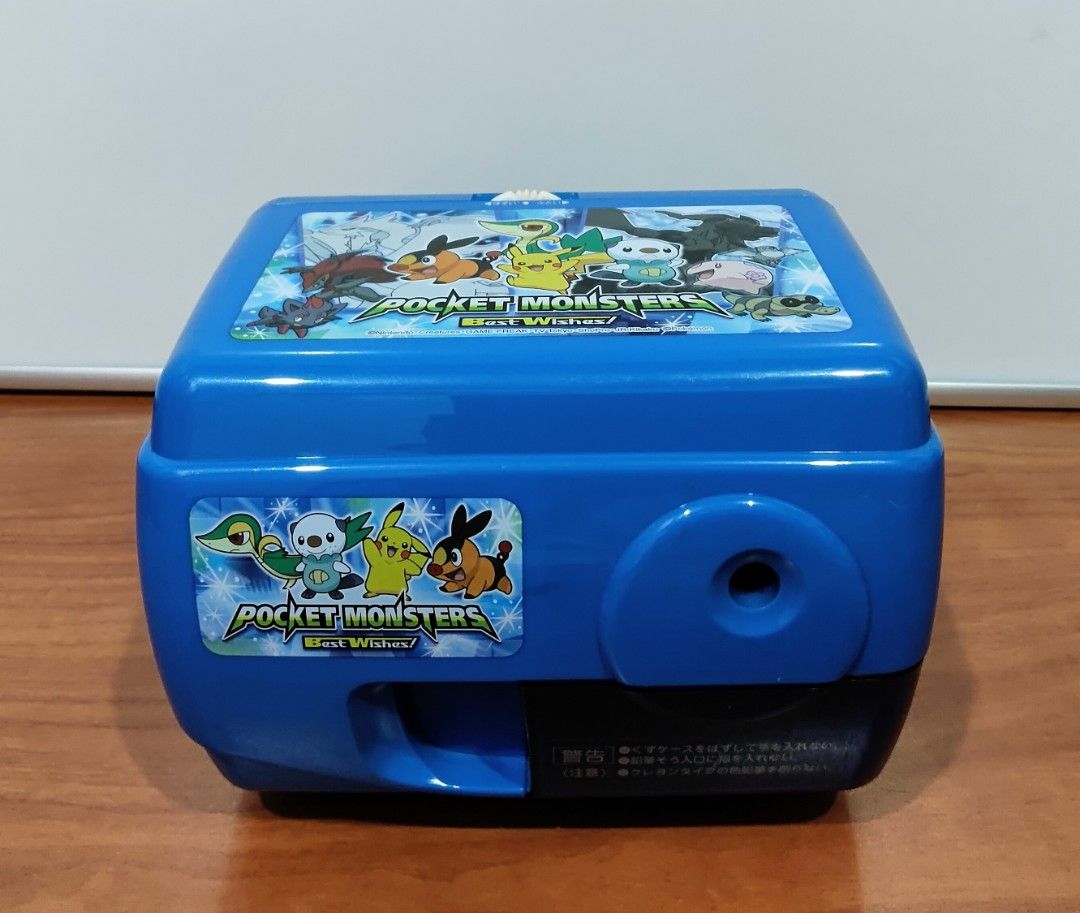 Pokemon Electric Pencil Sharpener (Category: Character Goods) located in Binangonan. Submitted by caaaris (Listing ID 1401669816, Image 2). Description: Electric pencil sharpener featuring a Pokemon design. It has a blue body with Pokemon graphics on the top and front. The sharpener has a pencil insertion hole and a compartment for shavings. It includes a power cord and a plug. The bottom has suction cups for stability. 100 volts. The model numbe