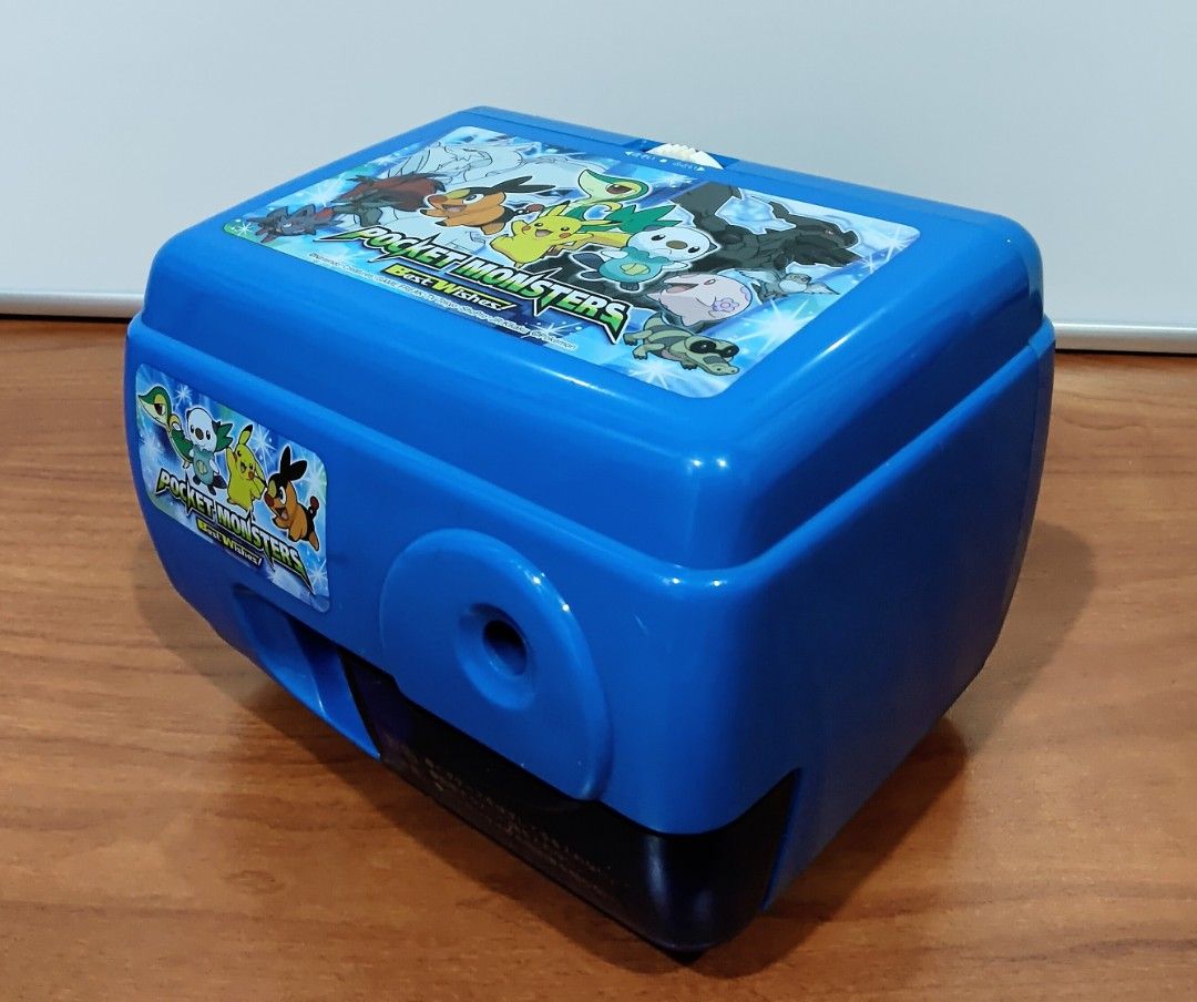 Pokemon Electric Pencil Sharpener (Category: Character Goods) located in Binangonan. Submitted by caaaris (Listing ID 1401669816, Image 1). Description: Electric pencil sharpener featuring a Pokemon design. It has a blue body with Pokemon graphics on the top and front. The sharpener has a pencil insertion hole and a compartment for shavings. It includes a power cord and a plug. The bottom has suction cups for stability. 100 volts. The model numbe