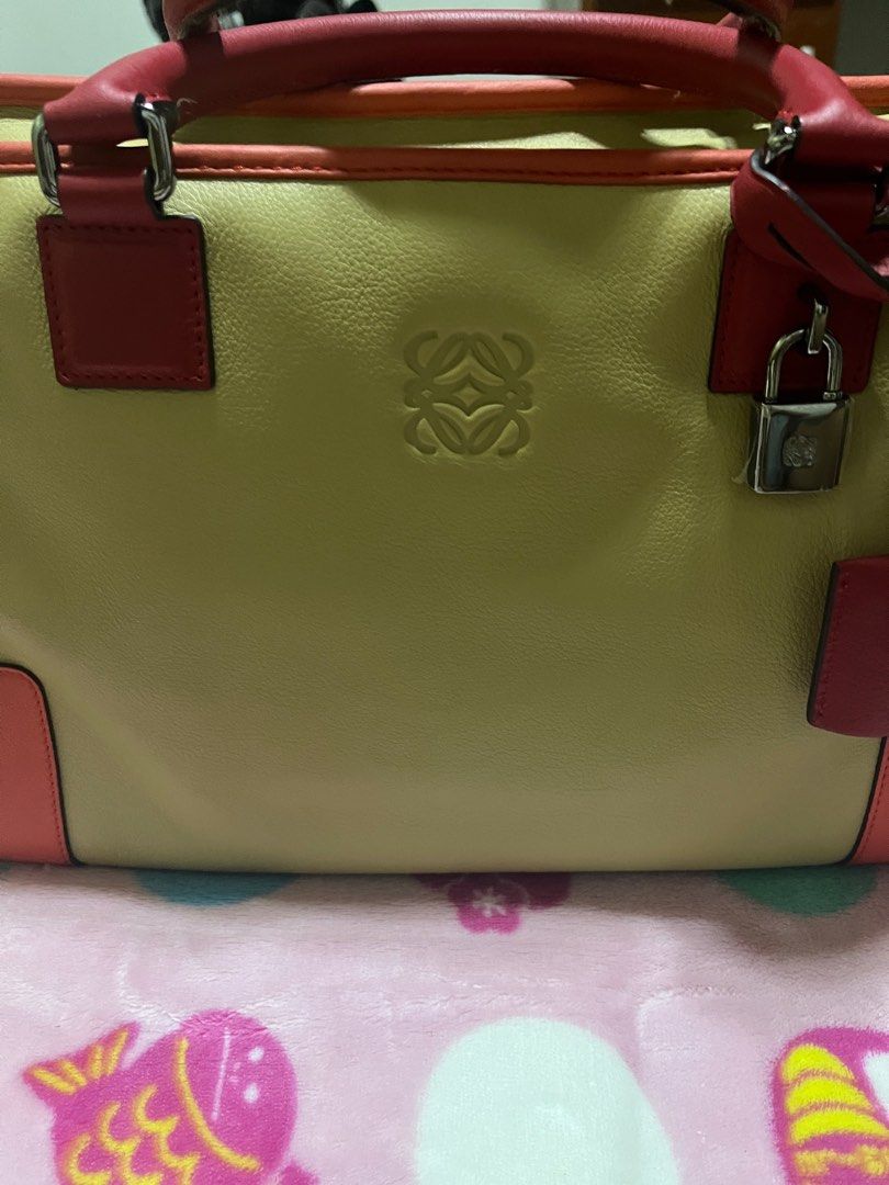 Loewe Amazona Handbag (Category: Luxury Bags & Wallets) located in Iloilo. Submitted by uapskie (Listing ID 1403393528, Image 2). Description: - Authentic Loewe Amazona handbag - Color: Beige and Red - Top handle design - Includes padlock with keys and dust bag - Secure zipper closure - Loewe logo visible - Protective metal feet at the bottom.