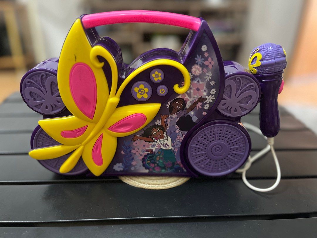 Encanto Karaoke Machine with Microphone (Category: Microphones) located in Calamba. Submitted by thepinkpicksee (Listing ID 1403572677, Image 1). Description: Encanto-themed karaoke machine features a butterfly design and comes with a wired microphone. It has speakers on both sides and a handle for easy carrying. The machine has buttons for music control and features images of characters from the movie. The back of the machine shows the model num