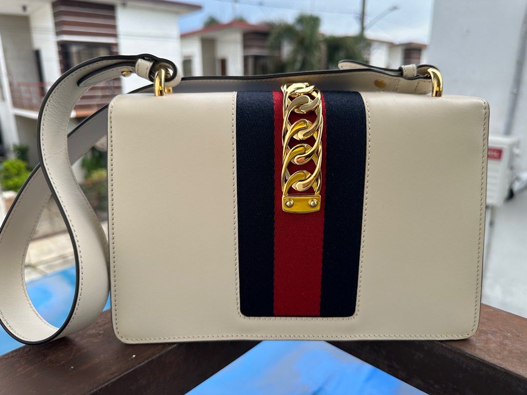 Gucci Sylvie Small Shoulder Bag (Authenticated by LegitGrails) (Category: Luxury Bags & Wallets) located in Manila. Submitted by kristineliban (Listing ID 1403645572, Image 3). Description: RFS: Need funds for home construction project With certificate of authenticity from LegitGrails Gucci Sylvie Small Shoulder Bag features a cream-colored leather exterior with a gold-tone chain and buckle closure. It has a signature red and navy stripe detail o
